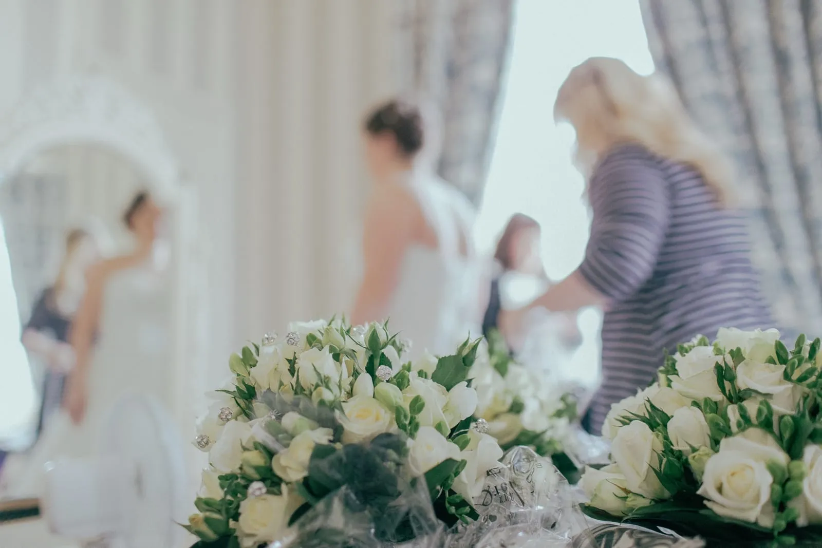 An out-of-focus wedding scene with a bride, an attendant, and white rose bouquets in the foreground